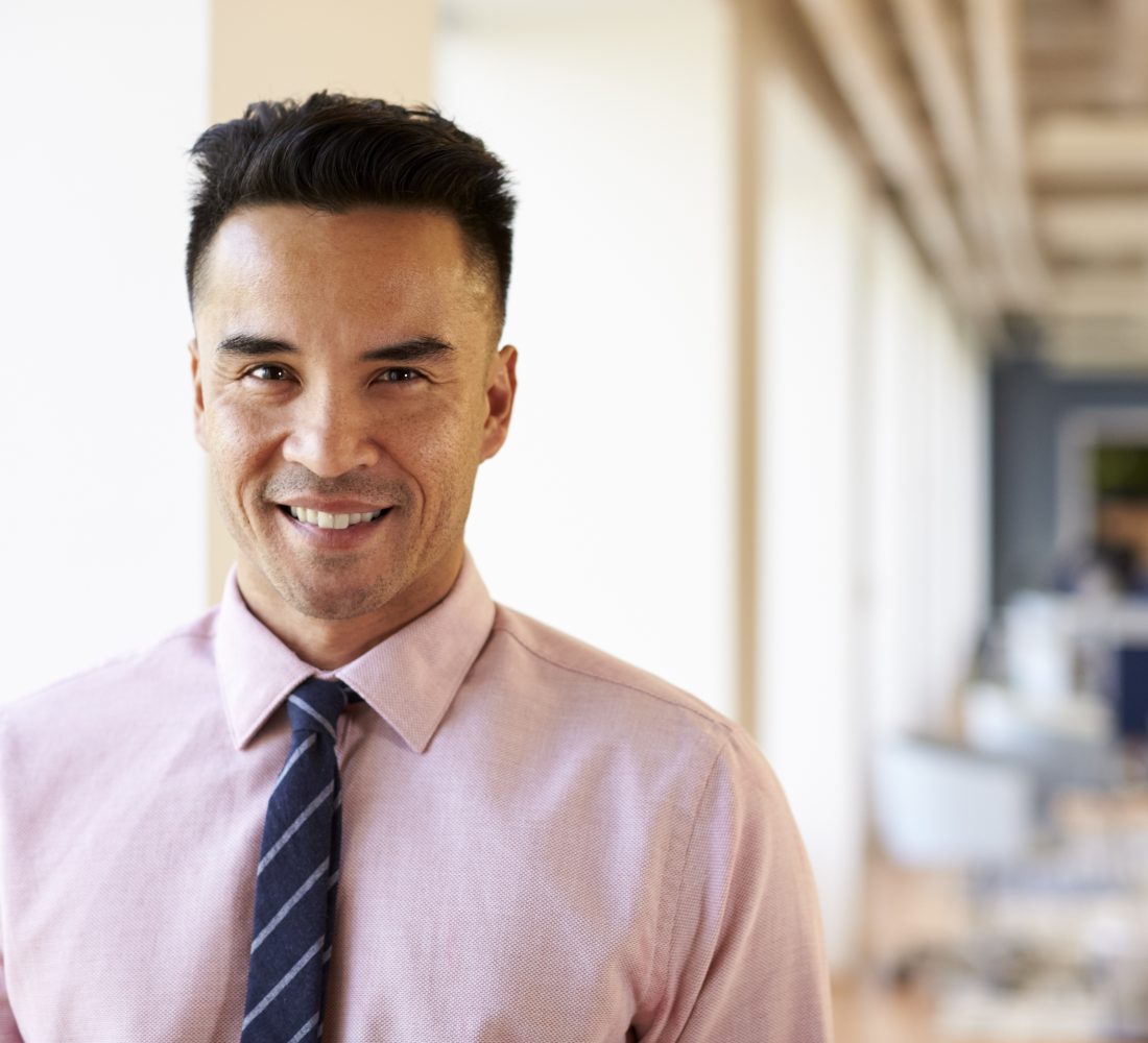 Portrait Of Smiling Mature Businessman In Modern Office Standing By Window